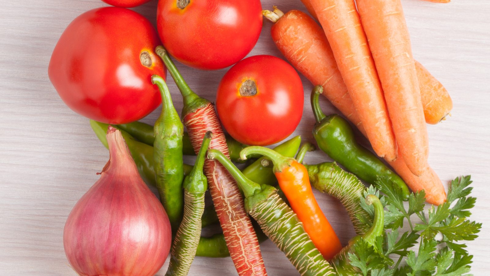 Fresh tomatoes, carrots, peppers, onions and parsley on a light wooden table